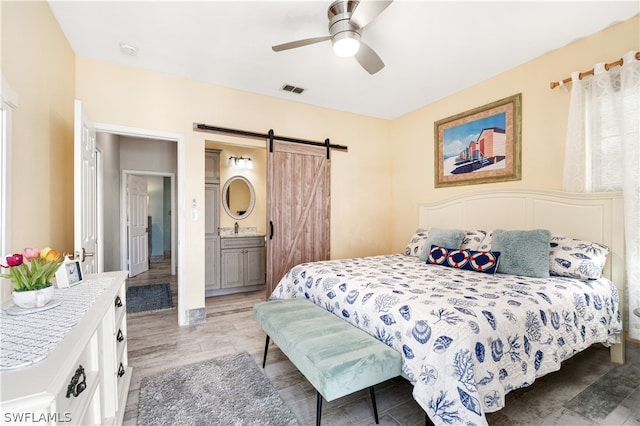 bedroom featuring hardwood / wood-style flooring, a barn door, sink, ensuite bathroom, and ceiling fan