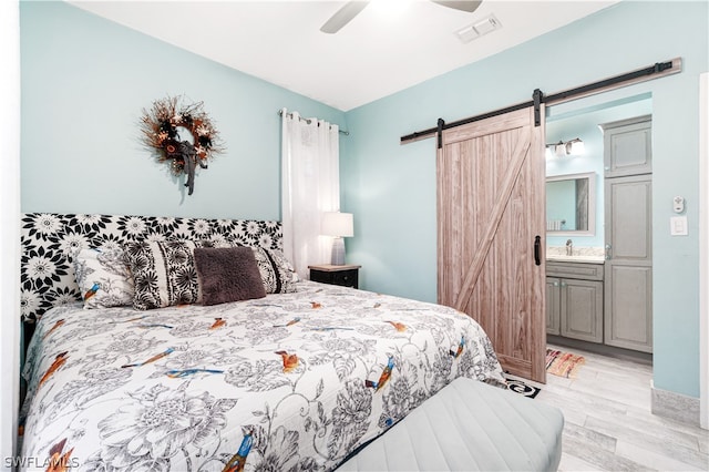 bedroom featuring light hardwood / wood-style flooring, ceiling fan, a barn door, sink, and ensuite bath