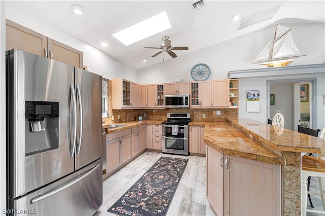 kitchen with ceiling fan, kitchen peninsula, vaulted ceiling with skylight, backsplash, and appliances with stainless steel finishes