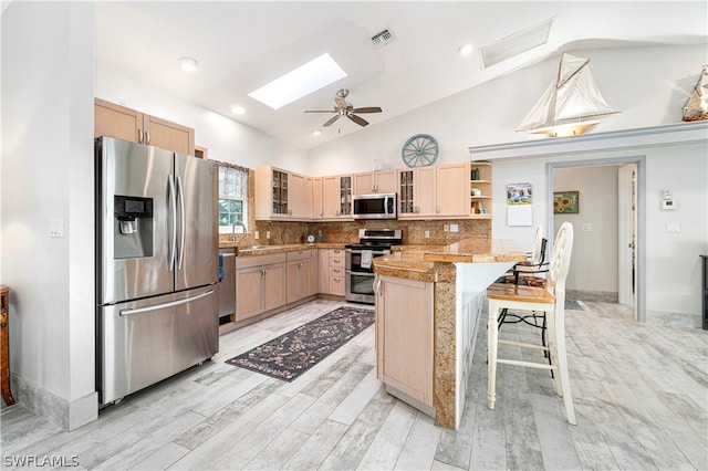 kitchen featuring a skylight, backsplash, ceiling fan, a breakfast bar area, and appliances with stainless steel finishes