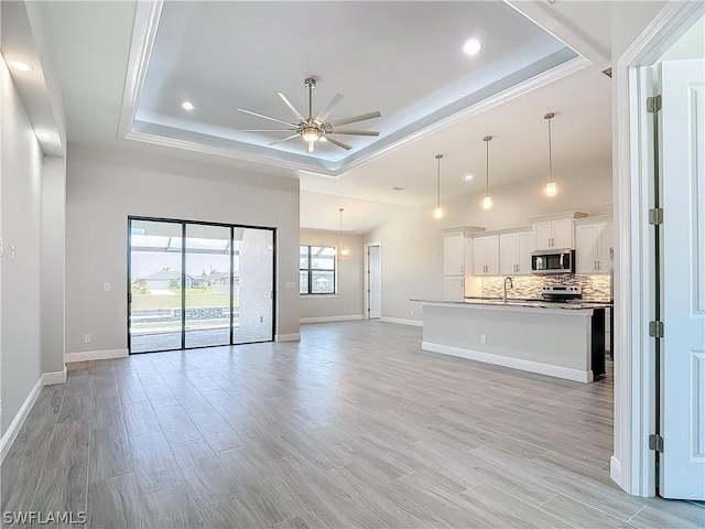 unfurnished living room featuring a raised ceiling, light wood-type flooring, sink, and ceiling fan