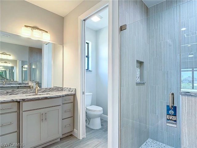 bathroom featuring a shower with door, vanity, and toilet