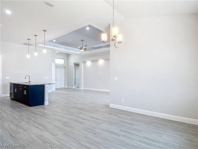 unfurnished living room with a raised ceiling, sink, and ceiling fan with notable chandelier