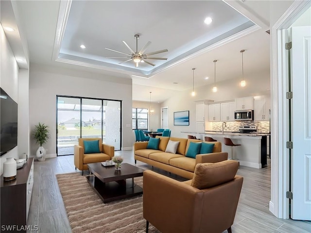 living room featuring ceiling fan, sink, a tray ceiling, and light hardwood / wood-style floors