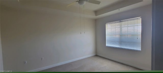 carpeted empty room with a raised ceiling and ceiling fan