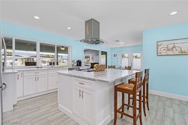 kitchen with a center island, light stone countertops, white cabinets, island exhaust hood, and sink