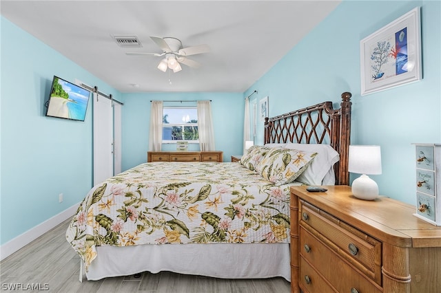 bedroom featuring a barn door, ceiling fan, and light hardwood / wood-style floors