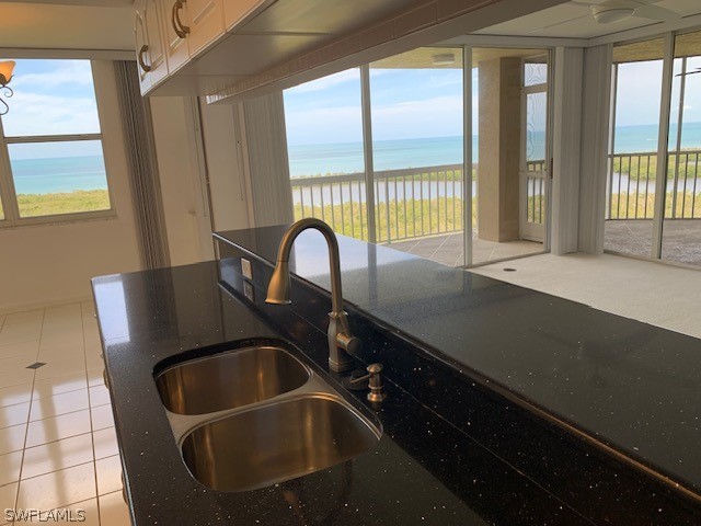 kitchen with light tile patterned floors, a healthy amount of sunlight, a water view, and sink