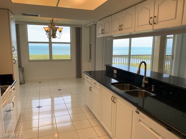 kitchen featuring dishwasher, sink, white cabinetry, a water view, and light tile patterned floors