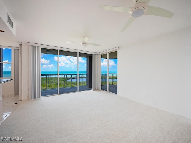 unfurnished room featuring visible vents, a ceiling fan, light colored carpet, a water view, and floor to ceiling windows