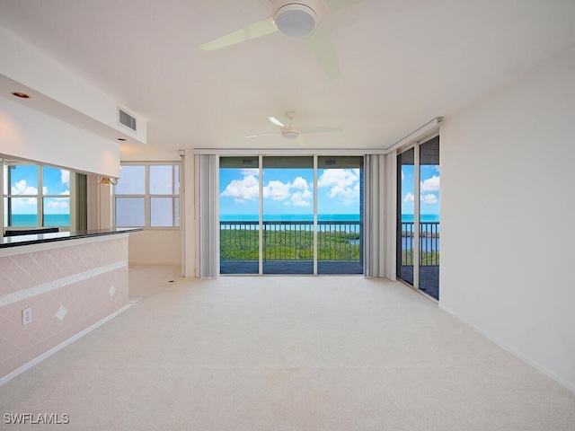 empty room with light carpet, a water view, a ceiling fan, visible vents, and floor to ceiling windows