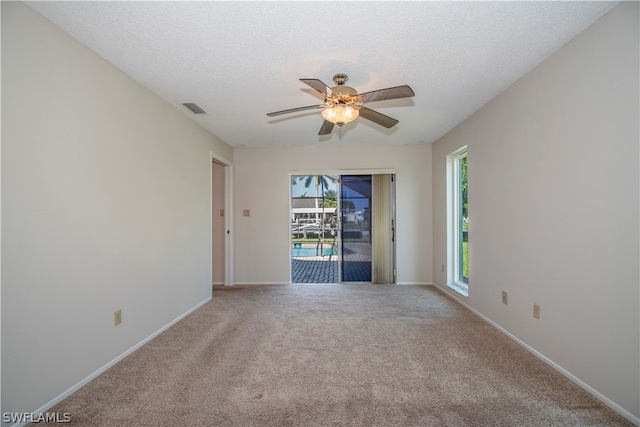 carpeted empty room featuring a textured ceiling, a wealth of natural light, and ceiling fan