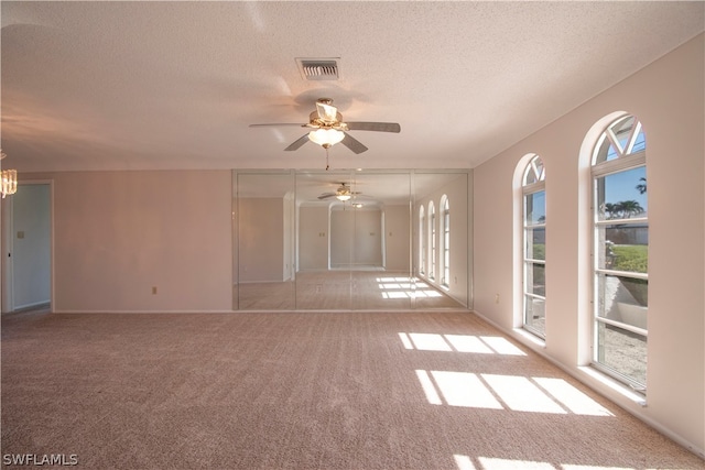 carpeted spare room with plenty of natural light, ceiling fan, and a textured ceiling