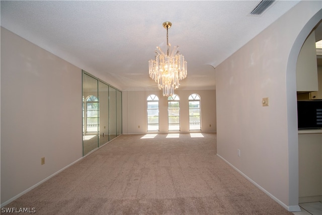 empty room featuring a textured ceiling, carpet, and an inviting chandelier