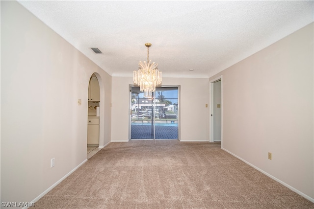 carpeted empty room featuring a textured ceiling and an inviting chandelier