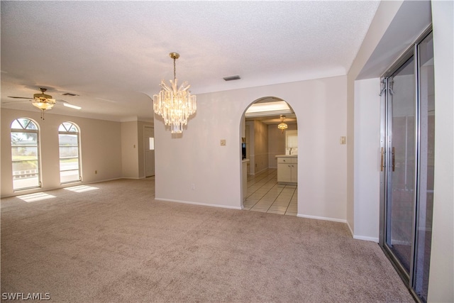 carpeted spare room featuring ceiling fan with notable chandelier and a textured ceiling