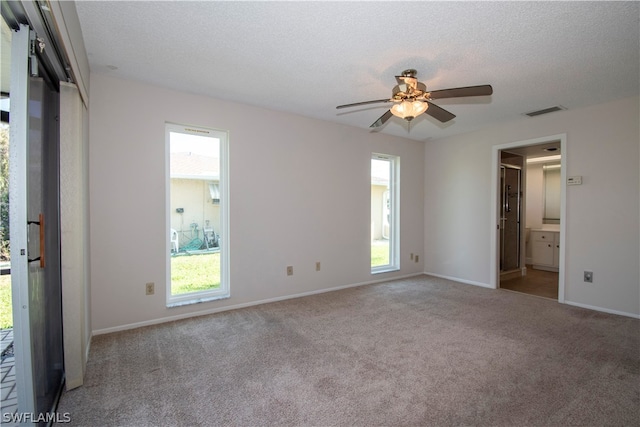 unfurnished bedroom featuring ensuite bath, carpet floors, ceiling fan, and multiple windows