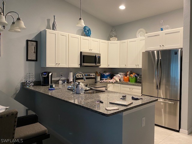 kitchen featuring decorative light fixtures, kitchen peninsula, white cabinets, and stainless steel appliances