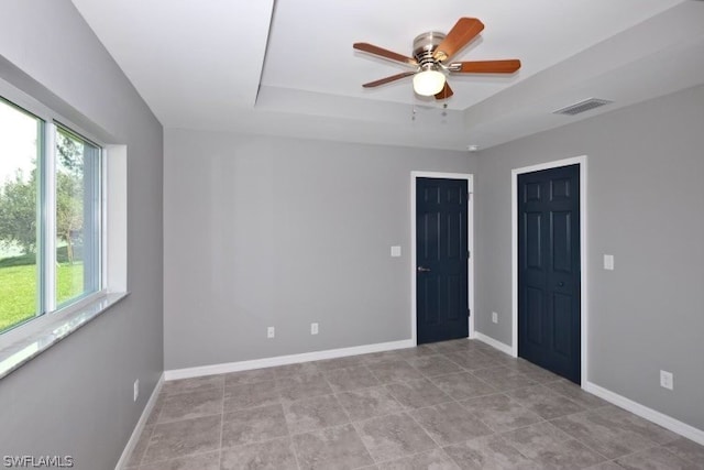 unfurnished bedroom featuring a raised ceiling, ceiling fan, light tile floors, and multiple windows