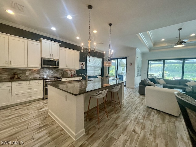 kitchen featuring an island with sink, light hardwood / wood-style floors, ceiling fan with notable chandelier, and stainless steel appliances