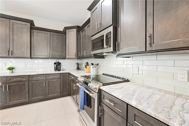 kitchen with dark brown cabinetry, appliances with stainless steel finishes, light tile flooring, backsplash, and light stone countertops