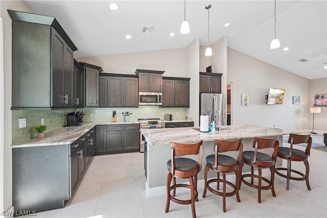 kitchen featuring a kitchen island with sink, hanging light fixtures, stainless steel appliances, light tile floors, and tasteful backsplash