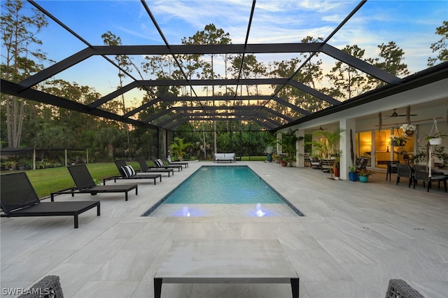 pool at dusk with a patio, a lanai, and pool water feature