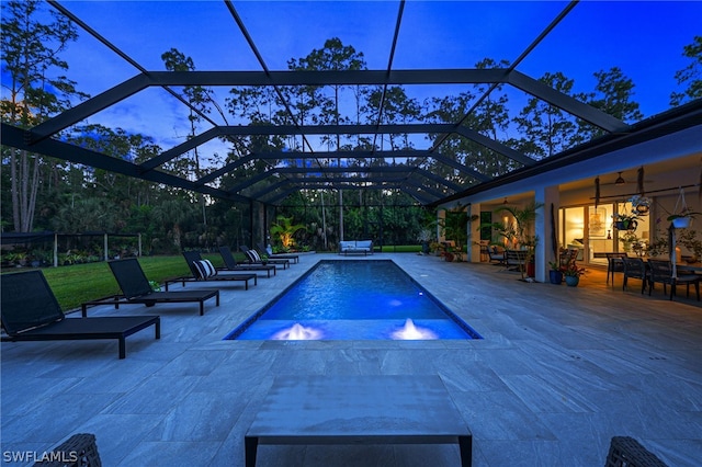 pool at dusk featuring a patio, pool water feature, a hot tub, and glass enclosure