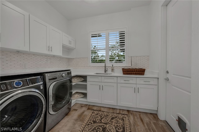 laundry area featuring sink, washing machine and clothes dryer, light wood-type flooring, and cabinets