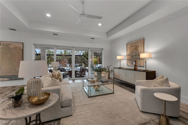 living room featuring ceiling fan, wood-type flooring, and a tray ceiling