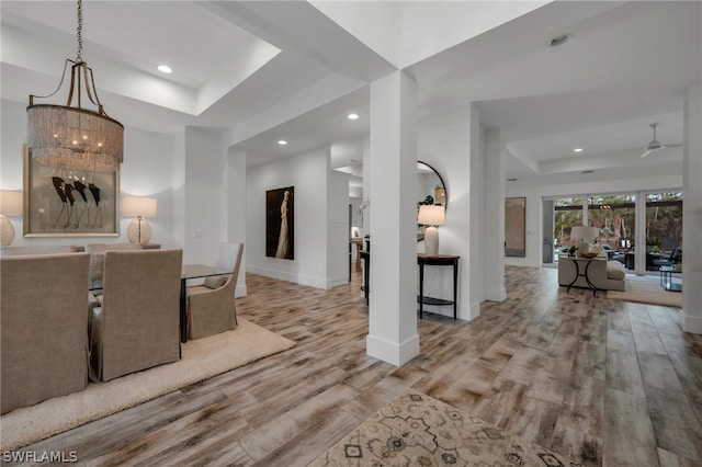 dining space with a raised ceiling, light hardwood / wood-style flooring, and ceiling fan with notable chandelier