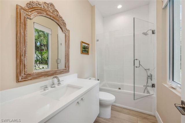 full bathroom with vanity, wood-type flooring, shower / bath combination with glass door, and toilet