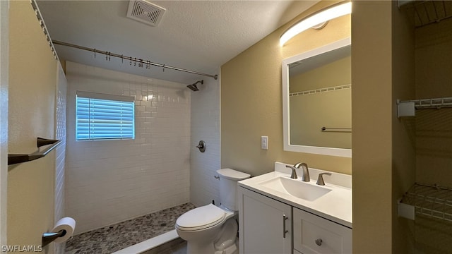 bathroom with toilet, vanity, a textured ceiling, and a tile shower