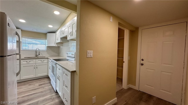 kitchen featuring white cabinetry, stainless steel refrigerator, sink, light wood-type flooring, and white range with electric cooktop