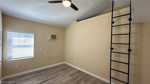 spare room featuring ceiling fan, lofted ceiling, a textured ceiling, hardwood / wood-style flooring, and a wall mounted AC