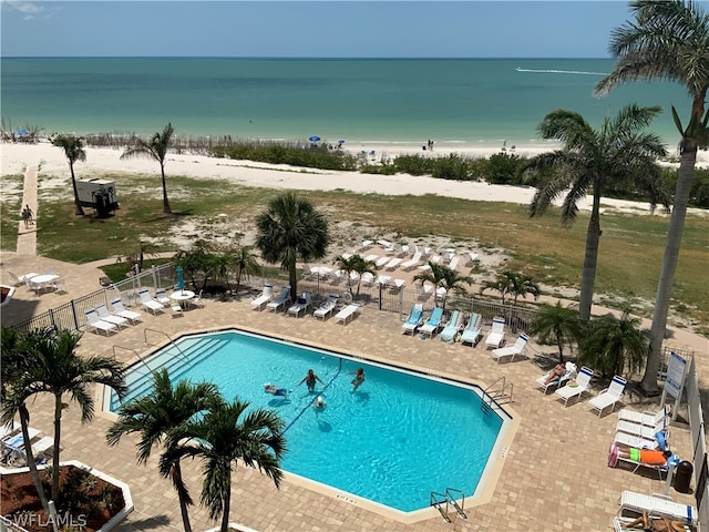 view of swimming pool with a patio, a water view, and a view of the beach