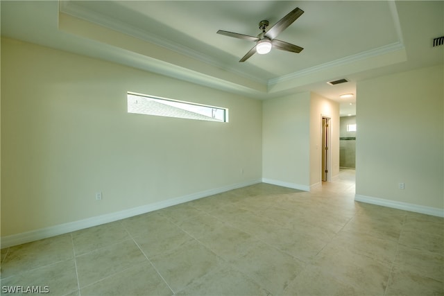 tiled empty room with ceiling fan, a tray ceiling, and ornamental molding