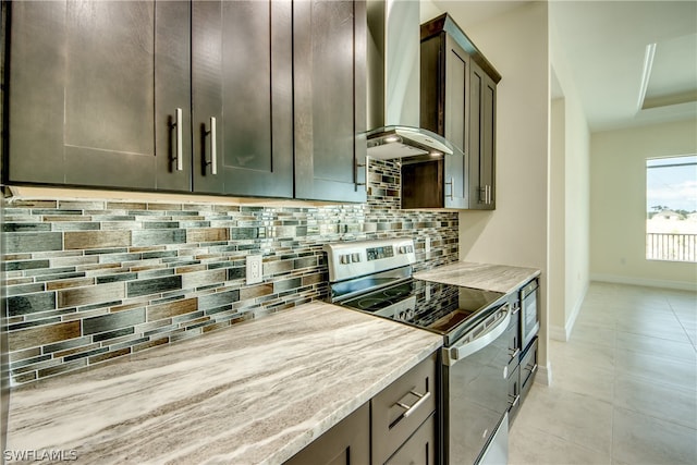 kitchen with wall chimney exhaust hood, backsplash, stainless steel electric stove, dark brown cabinets, and light stone countertops