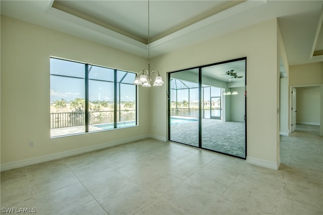 tiled empty room featuring a chandelier and a tray ceiling