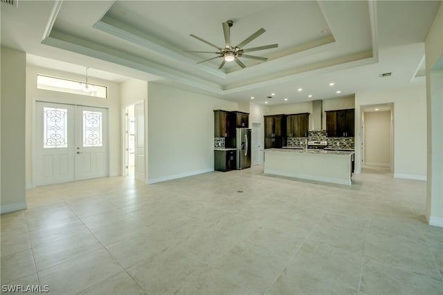 unfurnished living room with light tile flooring, french doors, ceiling fan, and a raised ceiling