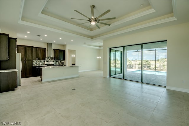 kitchen featuring a kitchen island with sink, backsplash, dark brown cabinets, a raised ceiling, and ceiling fan