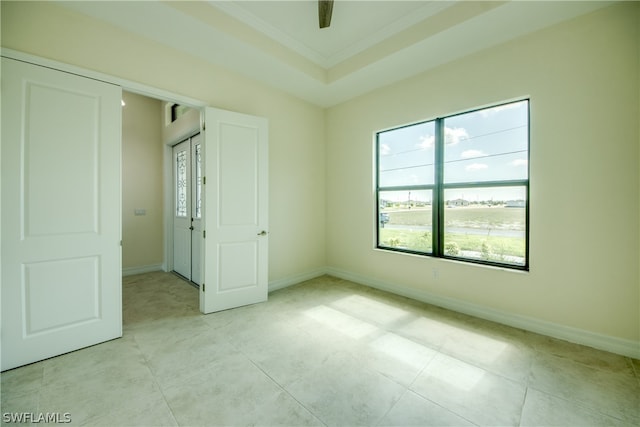 empty room with a raised ceiling, light tile floors, and ornamental molding