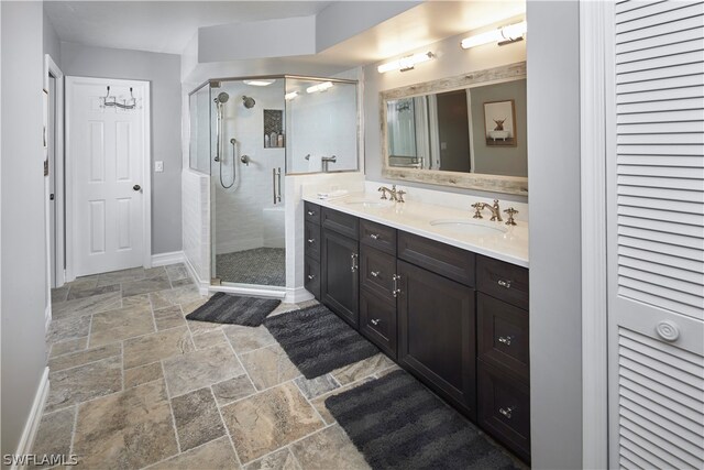 full bath featuring double vanity, a sink, stone tile flooring, and a shower stall