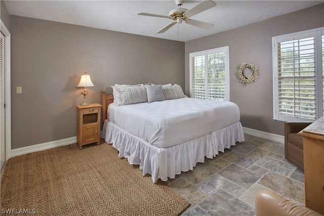 bedroom with a ceiling fan, stone tile flooring, and baseboards