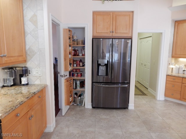 kitchen featuring light stone counters, stainless steel fridge with ice dispenser, and light tile patterned floors