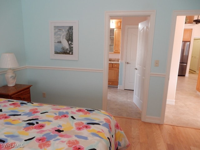 bedroom featuring stainless steel fridge, light hardwood / wood-style floors, and ensuite bathroom