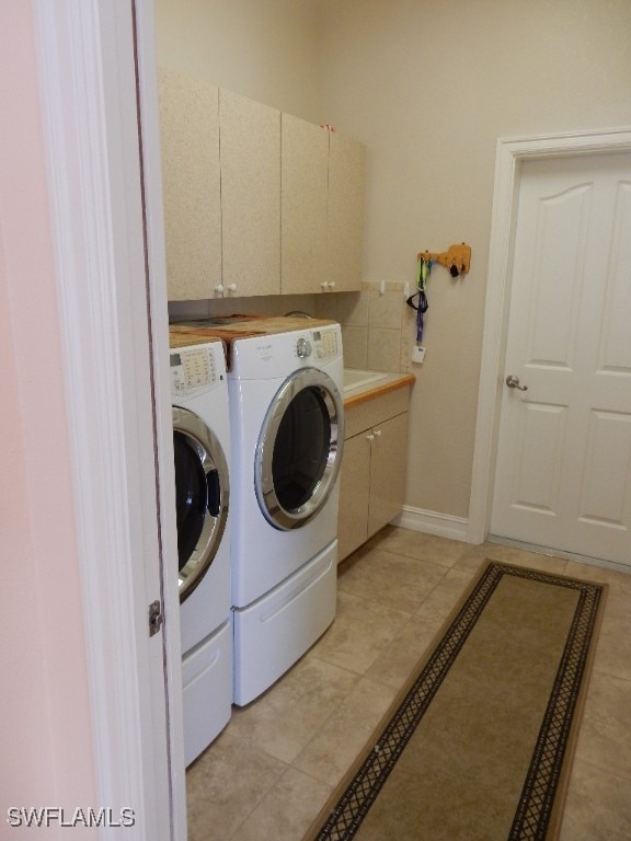 clothes washing area with light tile patterned flooring, cabinets, and washing machine and clothes dryer