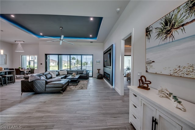 living room featuring ceiling fan, a tray ceiling, and light wood-type flooring