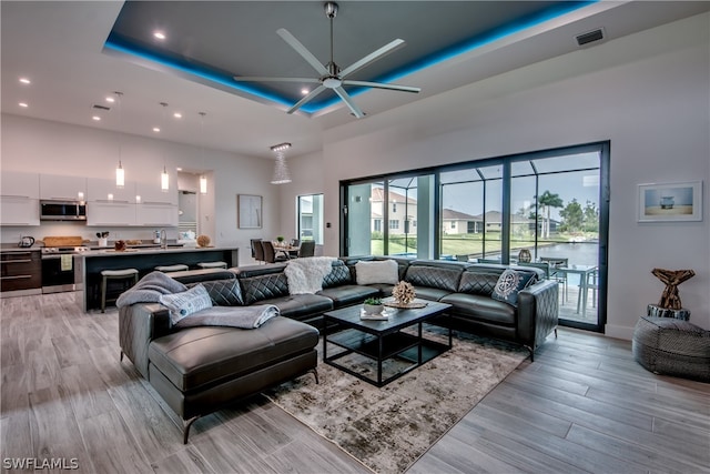 living room featuring ceiling fan, a towering ceiling, sink, light hardwood / wood-style floors, and a tray ceiling