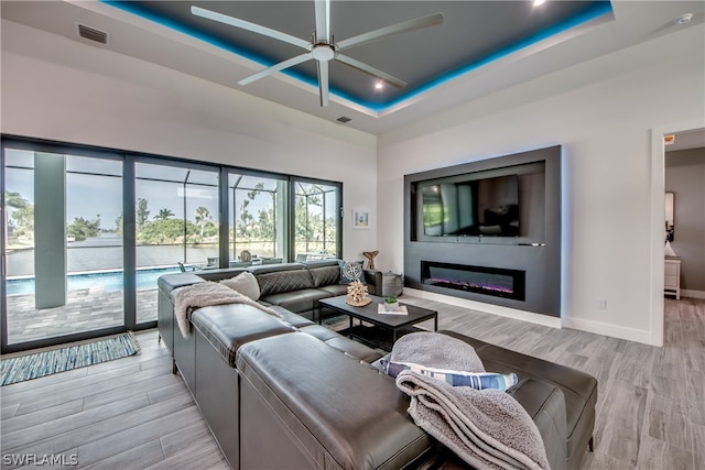 living room with light hardwood / wood-style floors, ceiling fan, and a tray ceiling